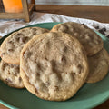 A plate of chocolate chip cookies on a green plate, set on a wooden table with a candle in the background.