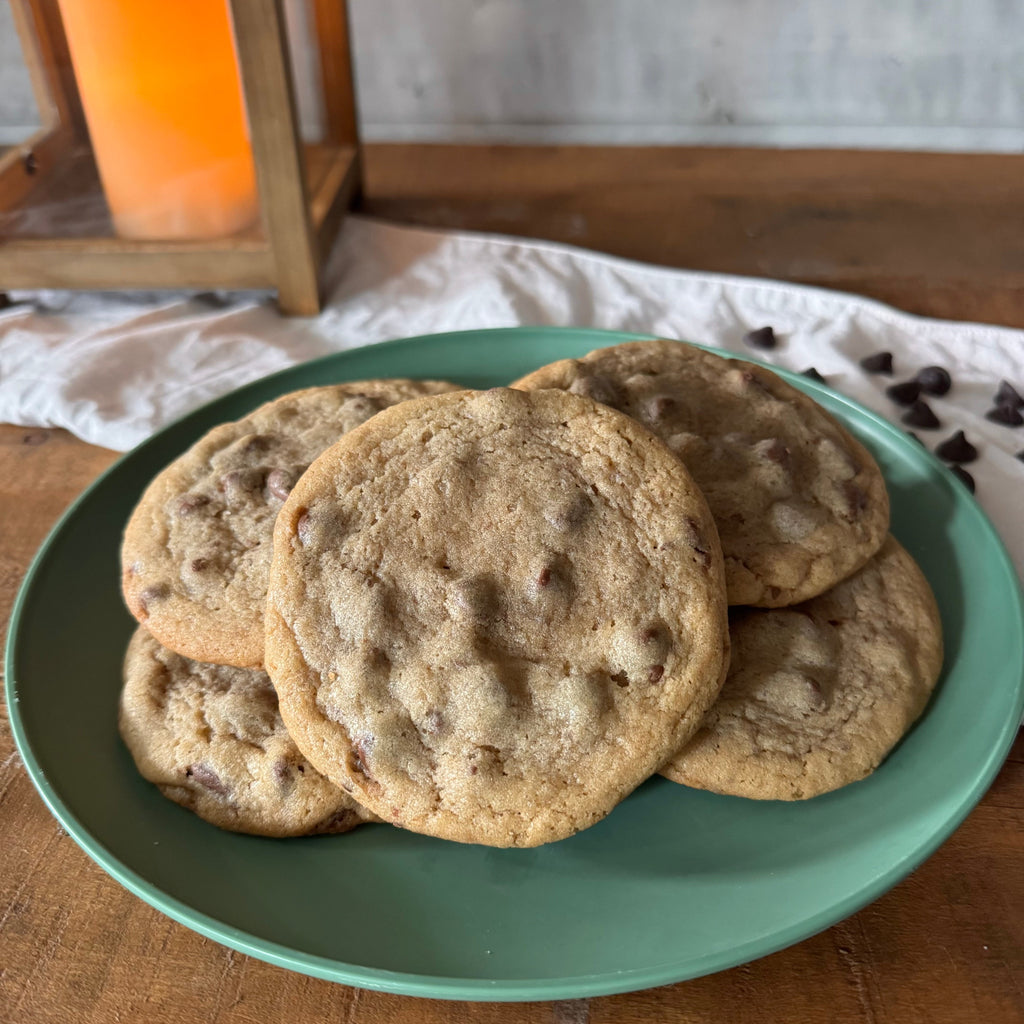 A stack of chocolate chip cookies on a mint green plate, set on a wooden table with a warm orange candle in the background.