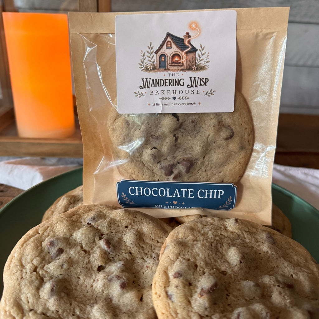 A package of Wandering Web Bakehouse chocolate chip cookies displayed on a green plate, with several cookies visible in front of the clear bag.