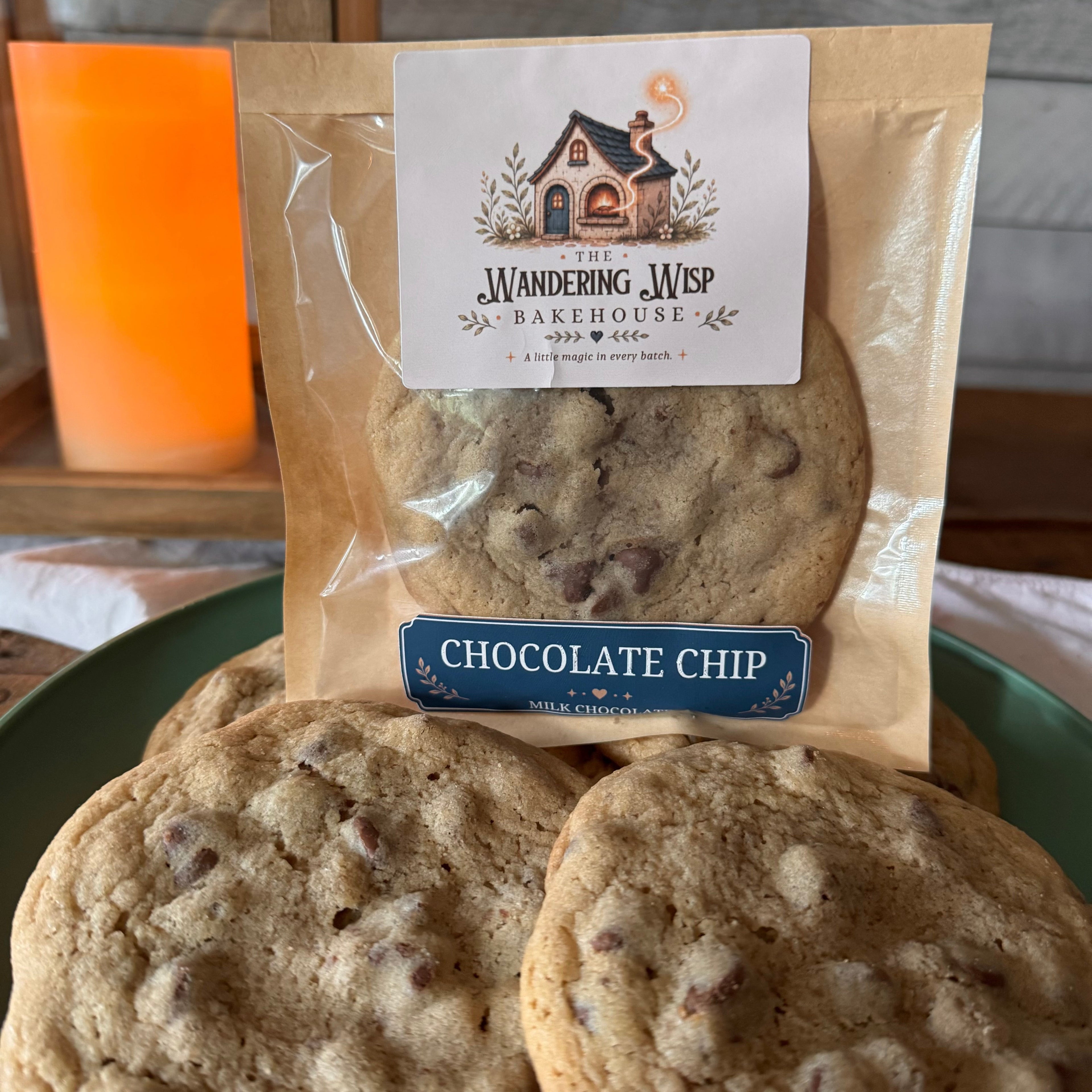 A package of Wandering Web Bakehouse chocolate chip cookies displayed on a green plate, with several cookies visible in front of the clear bag.