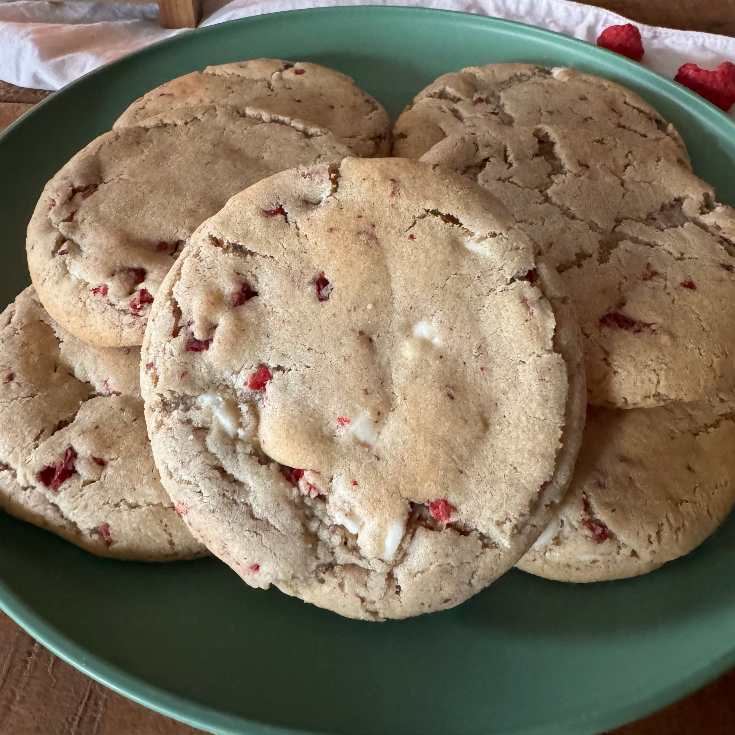 A close-up of several round raspberry and white chocolate cookies stacked on a green plate.
