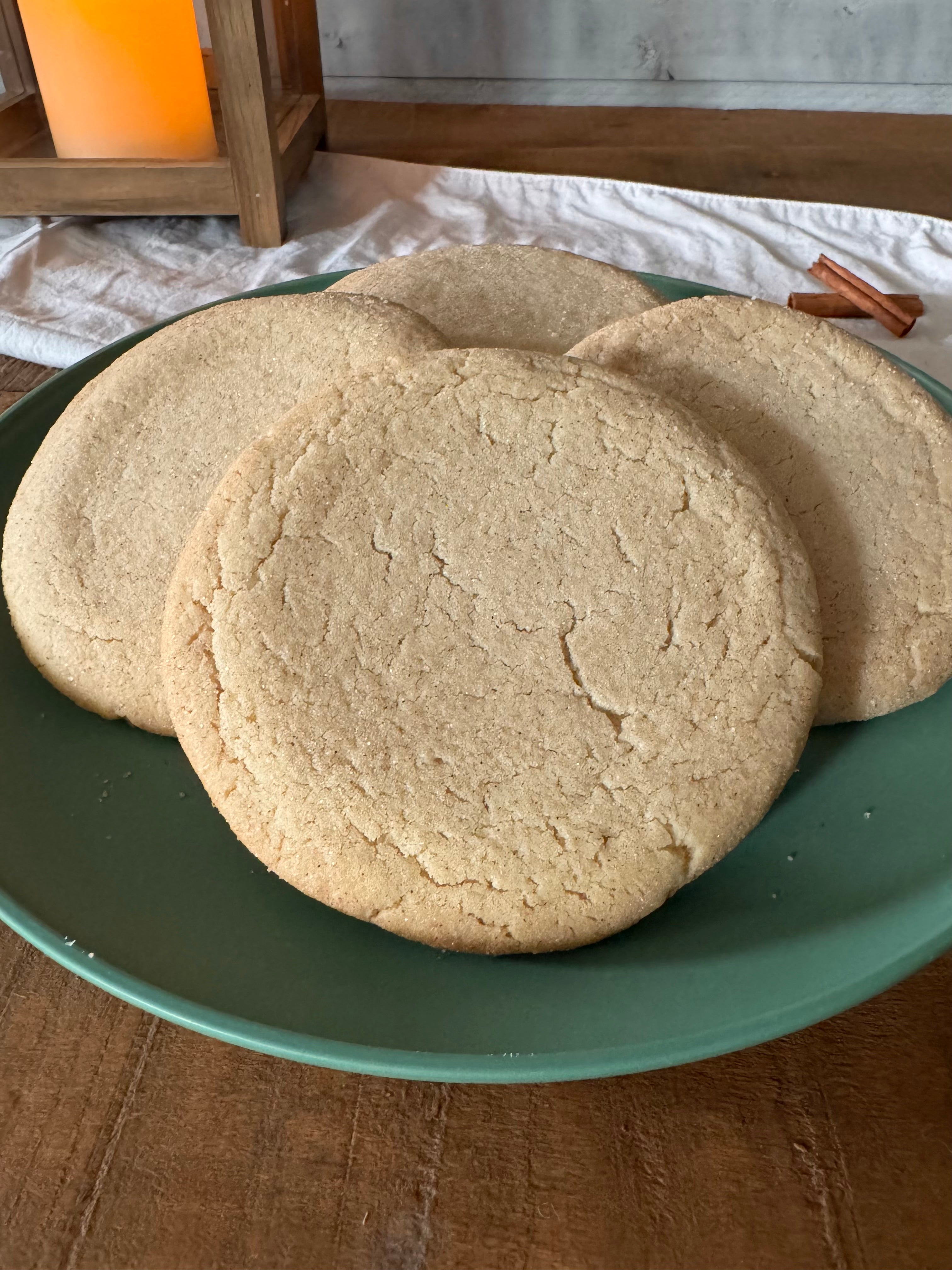 Snickerdoodle cookies on a green plate, set on a wooden table with a white cloth and a warm candle in the background.