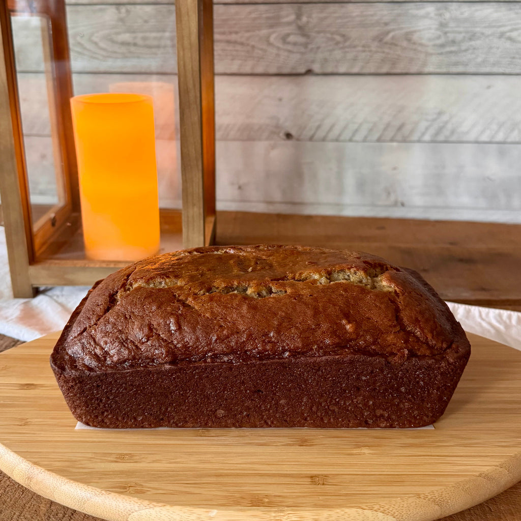 Whole loaf of classic banana bread photographed from the side on a wooden serving board with a warm lantern in the background.