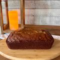 Whole loaf of classic banana bread photographed from the side on a wooden serving board with a warm lantern in the background.