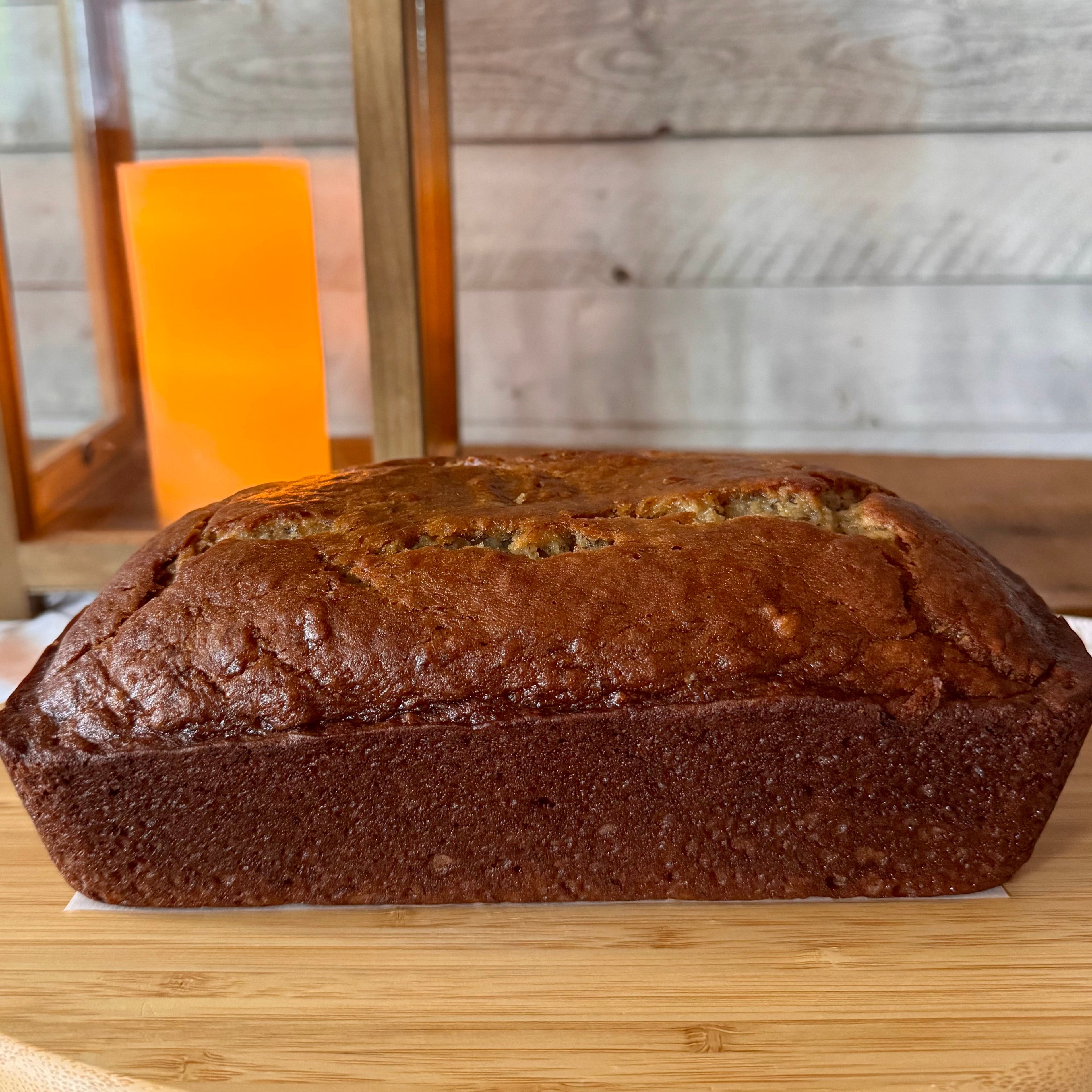 Freshly baked classic banana bread loaf on a wooden serving board with a warm lantern and rustic wood backdrop.