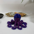 Glow-in-the-dark resin octopus sculpture with purple glitter body and blue glow head displayed on a white table.