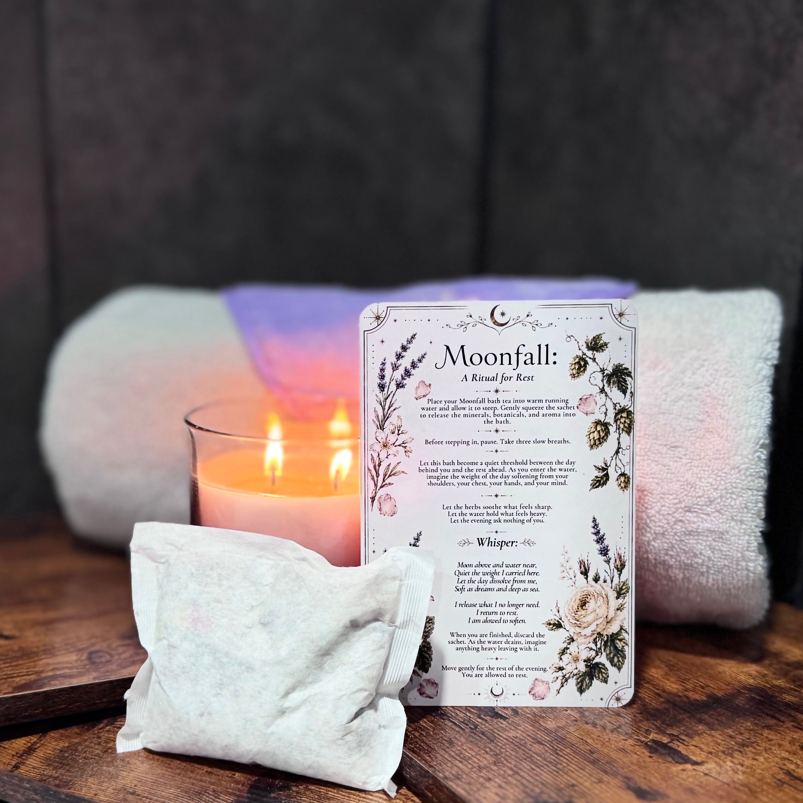 Bath products including a candle, ritual card and bath tea bag on a wooden shelf by a bathtub.