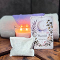 Candle, bath tea bag, and ritual card titled 'Moonfall' on a wooden surface with a dark background
