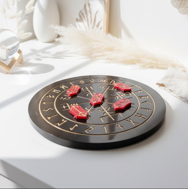 Red resin rune stones with gold inlays arranged on a black and red casting board with gold symbols
